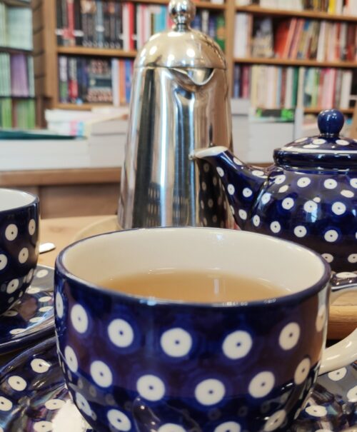 Dark blue spotted porcelain cups sit on a wooden table in front of a colourful shelf of books
