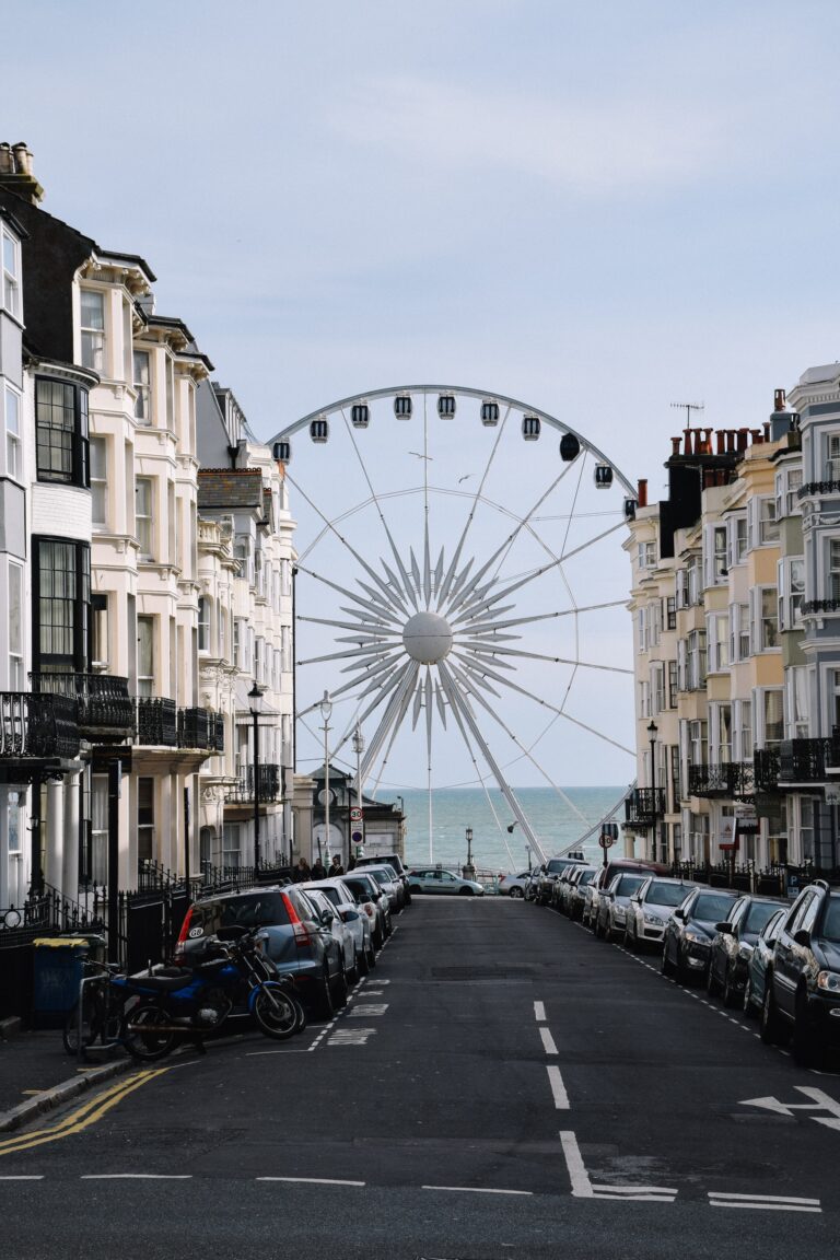 Terrace houses line the sides of a street. A big ferris wheel is stood at the end of the street in front of the ocean