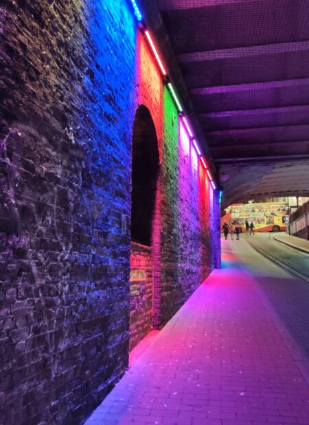 Colourful lights highlight the space under a dark bridge.