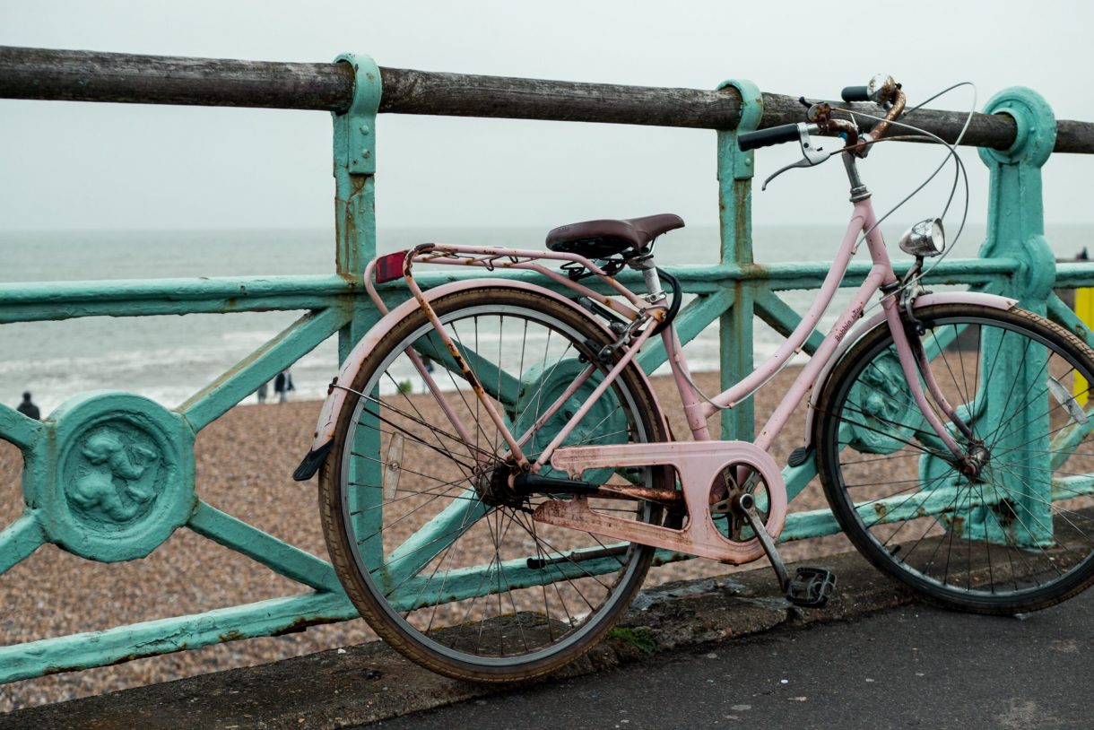 A hire bike leans against a turquoise fence. The beach is in the background