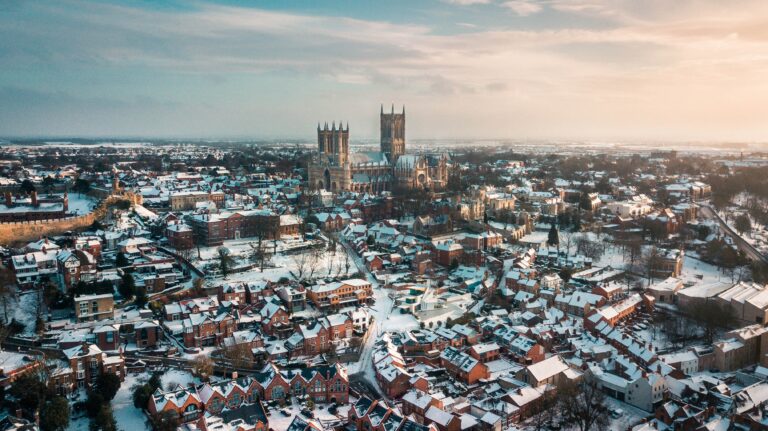 an aerial drone view of lincoln. The cathedral dominates the centre, castle walls snake along the left hand side and brown triangle-roofed houses stand around