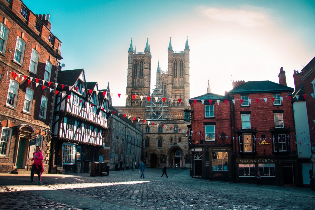 A cobbled street square. Red and white triangle flags are strung across the square. Lincoln cathedral stands in the background