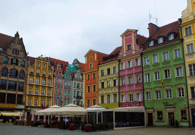 Colourful Polish Houses in yellow, pink and teal line a cobbled street. There are marquees outside restaurants.