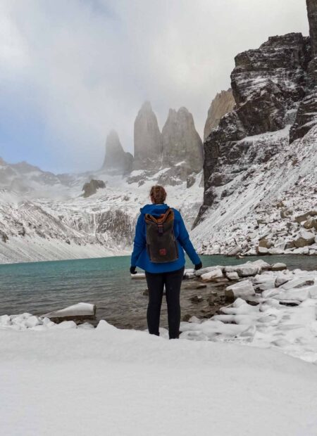 Alice stands in front of a mountain that looks like three towers, by a crystal blue lake