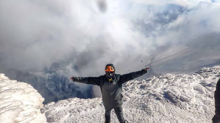 A man stands at the top of Villarrica Volcano in the snow/ the Volcano is smoking