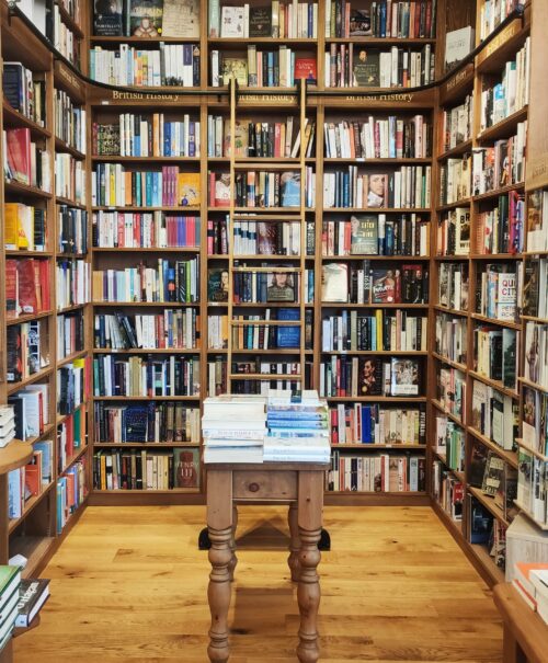 A brown ladder leans against colourful bookshelves in the British History section of at Toppings Bookshop