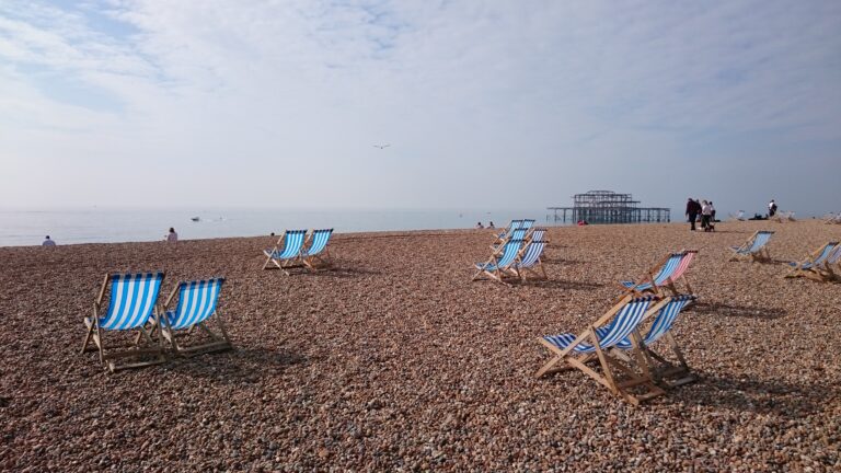 Striped blue and white deckchairs sit in pairs on a pebbled beach