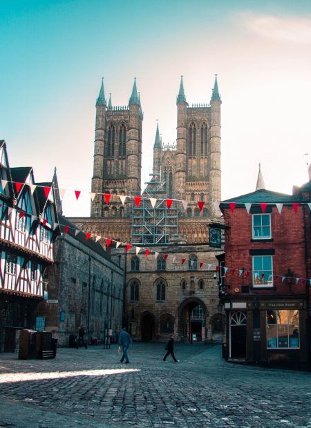 A cobbled street square. Red and white triangle flags are strung across the square. Lincoln cathedral stands in the background
