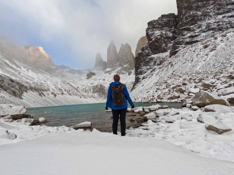 Alice stands in front of a mountain that looks like three towers, by a crystal blue lake